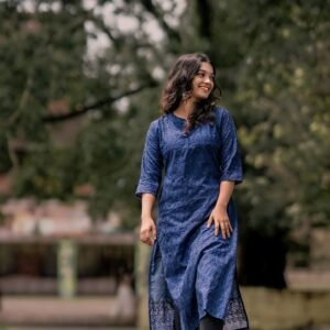 Woman in a blue kurti smiling and walking barefoot in a garden setting.
