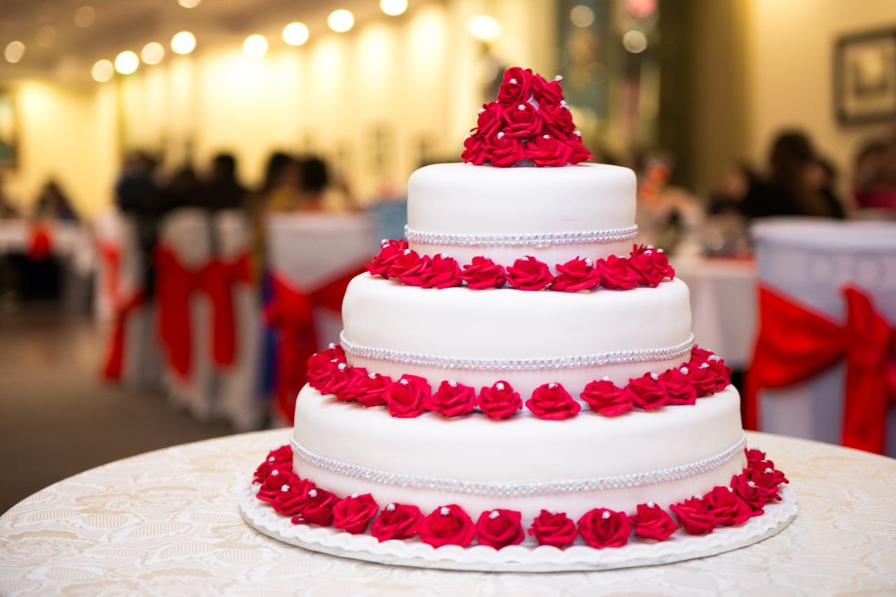 A stunning three-tier wedding cake adorned with vibrant red roses at a formal reception.
