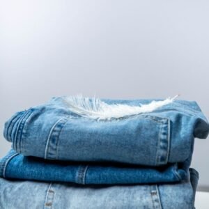A stack of blue denim jeans with a soft white feather on top against a white background.